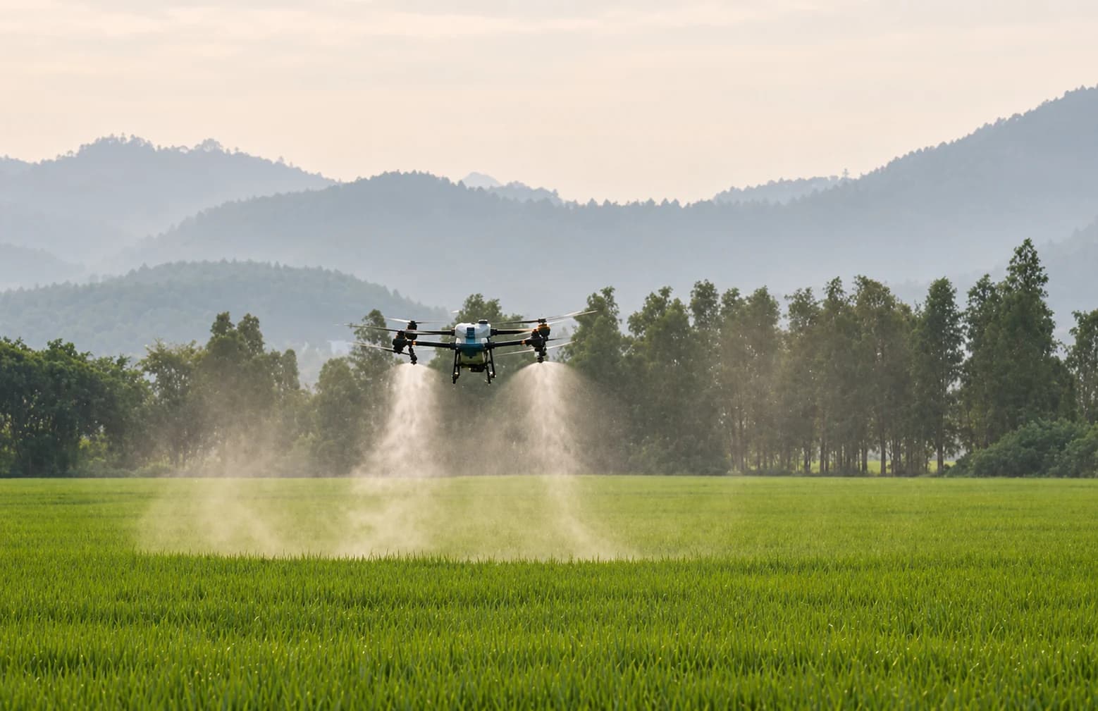 Agricultural drone spraying a green paddy field beneath tree-covered hills