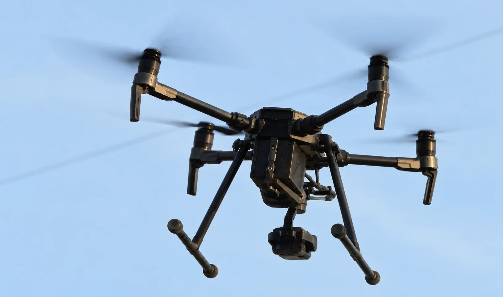 Lakshya prototype drone in flight with a suspended camera payload against a blue sky